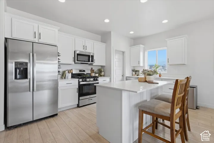Kitchen featuring white shaker-style cabinetry, a central island with a solid-surface countertop, stainless steel appliances, and wood-finish flooring
