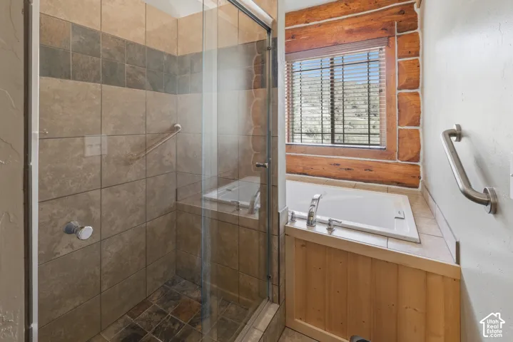 Glass-enclosed shower with tiled walls and floor, built-in shower bench, built-in soaking tub, and natural wood trim around the window