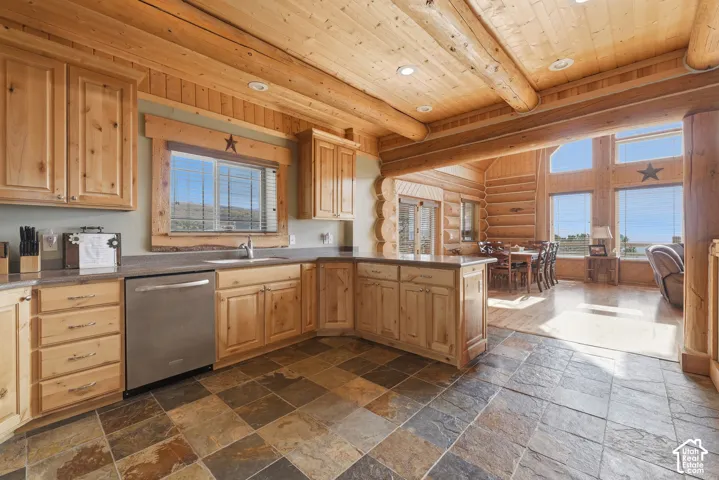Kitchen with natural wood cabinetry, stainless steel dishwasher, and a stone tile floor