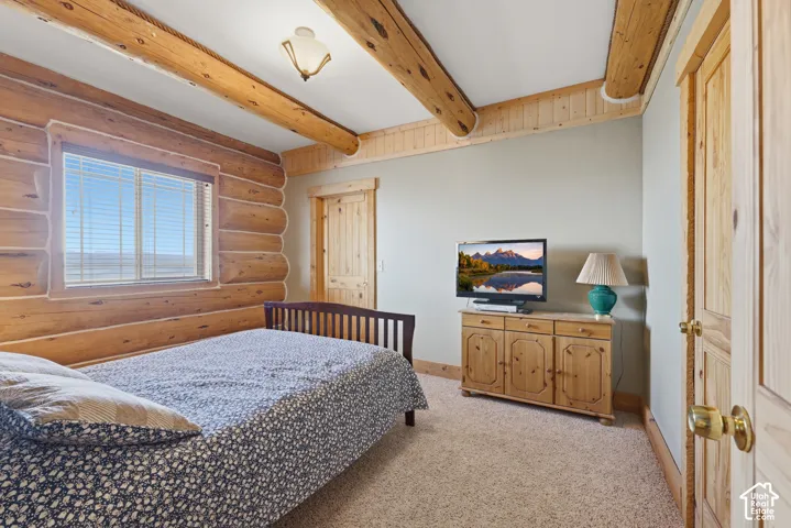 Log walls with exposed wood beams, wood-trimmed window, and carpeting