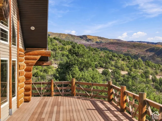 Expansive composite deck with horizontal wood railings and multiple levels, overlooking mature landscaping and forested hillside terrain