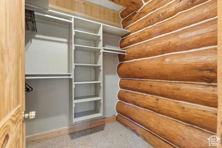 Built-in shelving and hanging rods, log wall construction, natural wood door, and carpeted flooring