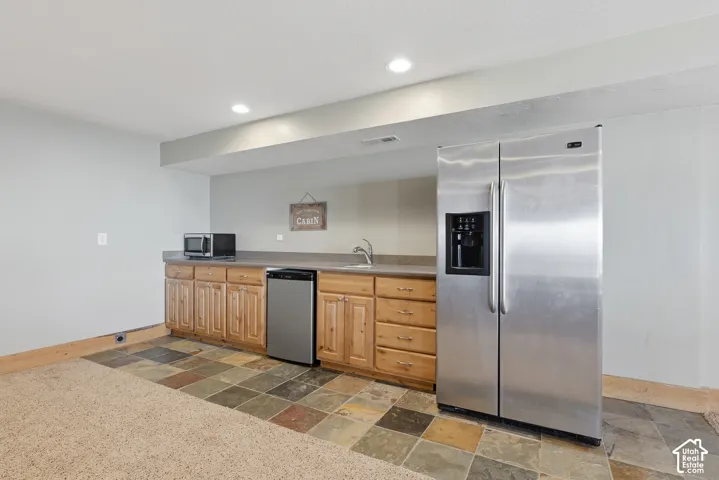 Built-in wet bar with wood cabinetry, stainless steel sink, and stone-look countertop