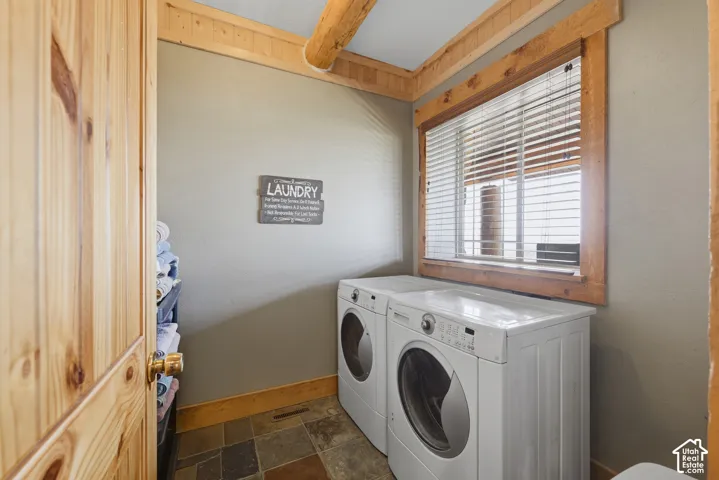 Laundry area featuring a window with wood trim, wood-finish ceiling beams, and tile flooring