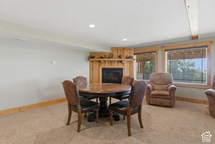 Corner fireplace with a wood surround, recessed lighting, wood-trimmed windows, and wood ceiling beams