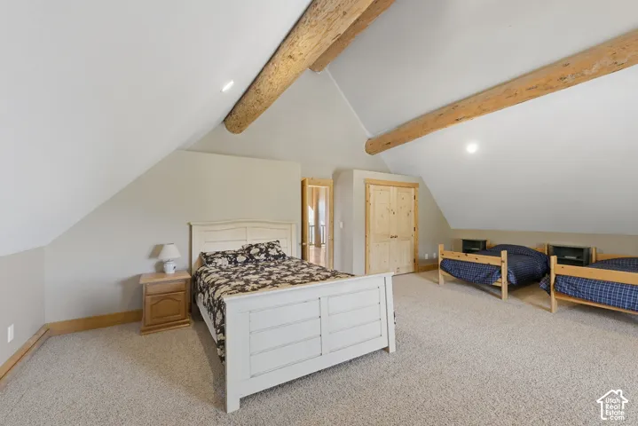 Angled ceiling with exposed wood beams, neutral carpeting, and light wood doors