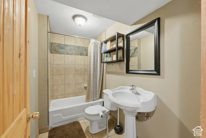 Pedestal sink with chrome faucet, tiled shower surround with accent band, white bathtub, and wood-paneled door