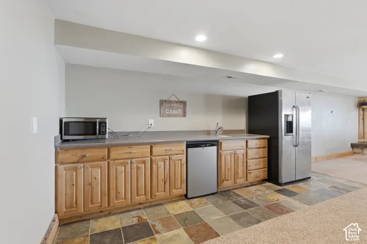 Kitchenette featuring wood cabinetry, stone-finish countertops, stainless steel appliances, and multi-tone tile flooring