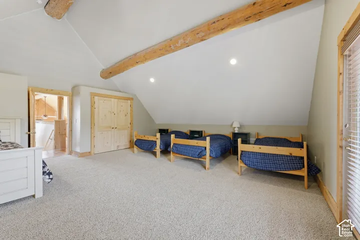 Vaulted ceiling with exposed wood beams, light-toned carpeting, wood-paneled doors, and recessed lighting