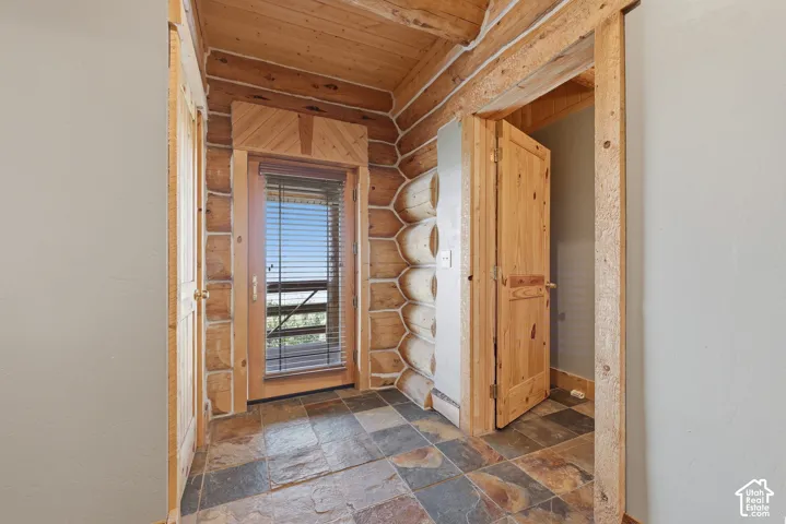 Rough-hewn log walls with natural wood beams, stone tile flooring, and a natural wood door