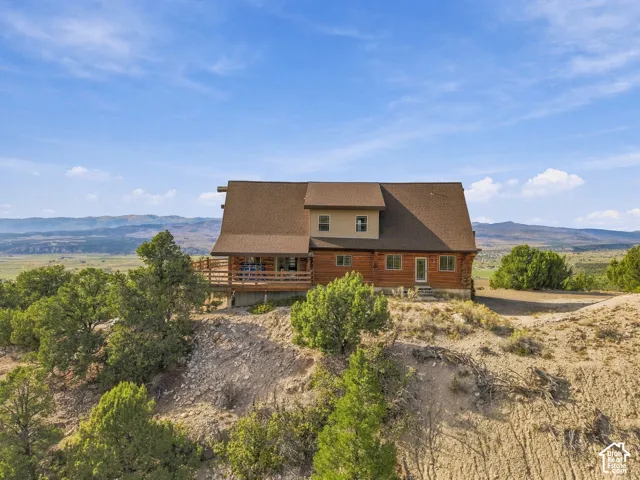 Log-sided home featuring a wrap-around deck, gabled roof, and a prominent hillside setting