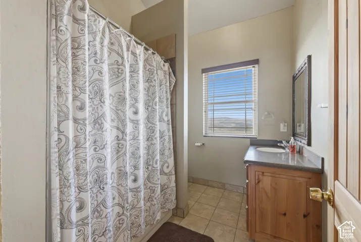 Tile flooring, wood vanity with integrated sink, framed mirror, and a window with horizontal blinds
