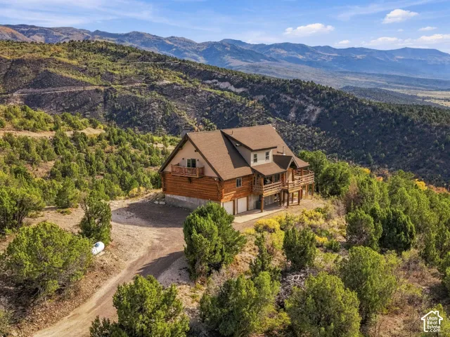 Multi-level log cabin-style residence featuring a two-car garage, multiple balconies, and a mountain backdrop