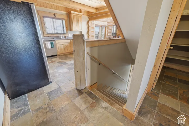 Stone-look tile flooring in a checkerboard pattern, natural wood cabinetry, stainless steel sink, wood-finish ceiling, and a wooden staircase with a handrail