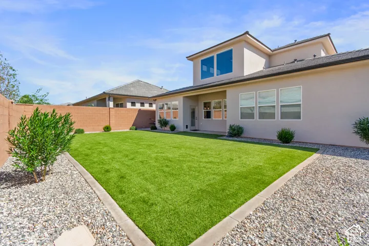 Expansive backyard with a manicured lawn, gravel perimeter, mature shrubs, and a stucco exterior