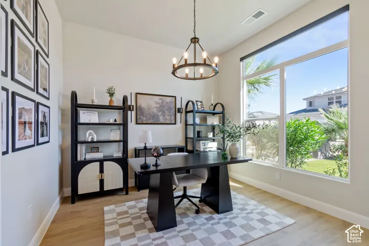 High ceilings with a decorative chandelier, expansive windows with a roller shade, wood-finish flooring, and built-in shelving units