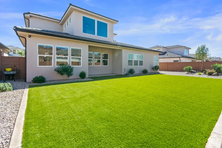 Expansive green lawn with a stucco exterior, multiple windows, gravel landscaping, and a privacy fence