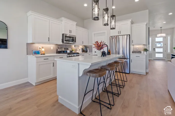 Kitchen featuring white cabinetry, stainless steel appliances, a center island with seating, pendant lighting, and wood-finish flooring