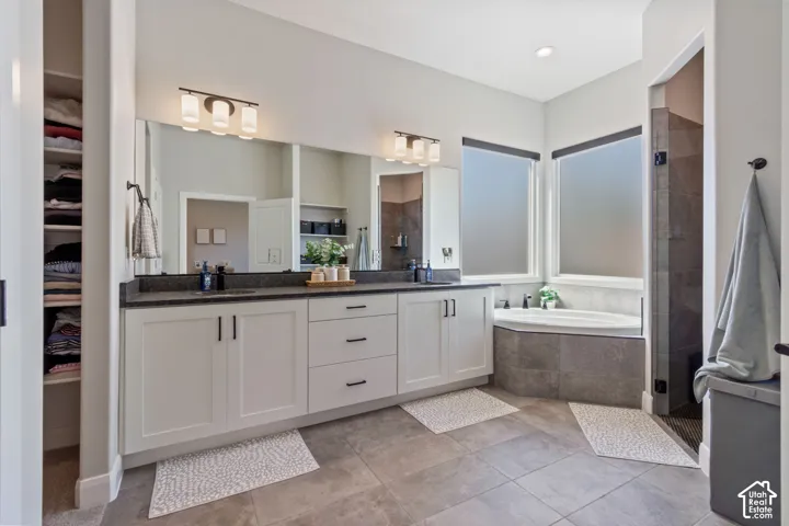 Dual vanity with dark countertops, a built-in corner bathtub, a glass-enclosed shower, and large format tile flooring