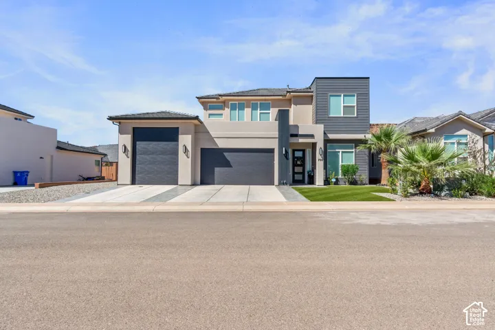 Modern exterior featuring a prominent two-car garage, contemporary dark gray siding, a stucco finish, and a well-maintained lawn with landscaping