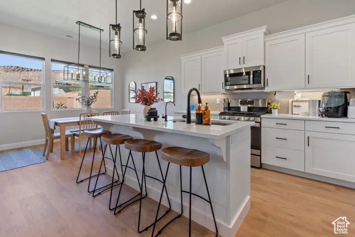 Open-concept kitchen with white shaker-style cabinetry, stainless steel appliances, and a kitchen island featuring a sink