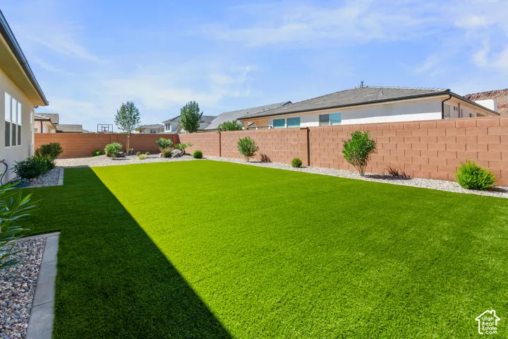 Expansive backyard featuring artificial turf, a low-maintenance gravel border, and a durable block perimeter fence