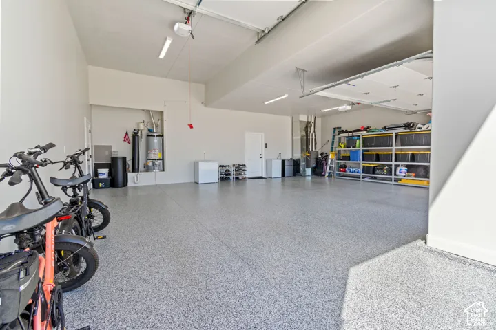 Spacious garage featuring a durable speckled epoxy floor, overhead lighting, and built-in water heater alcove