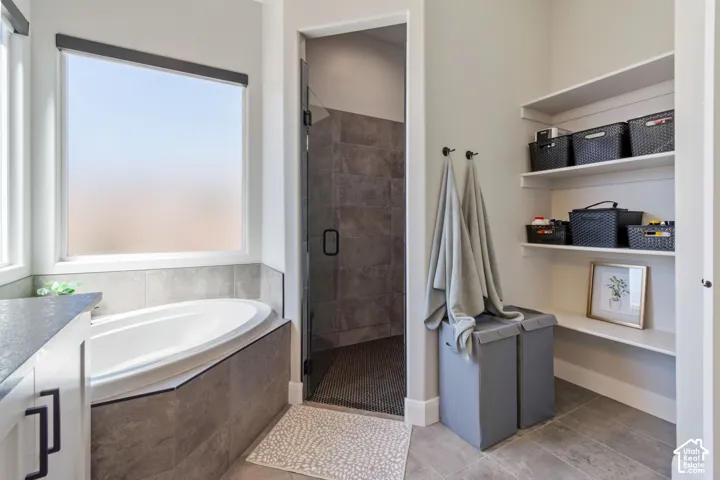 Soaking tub with tiled surround, glass-enclosed shower, wall-mounted shelving, and large window with privacy film