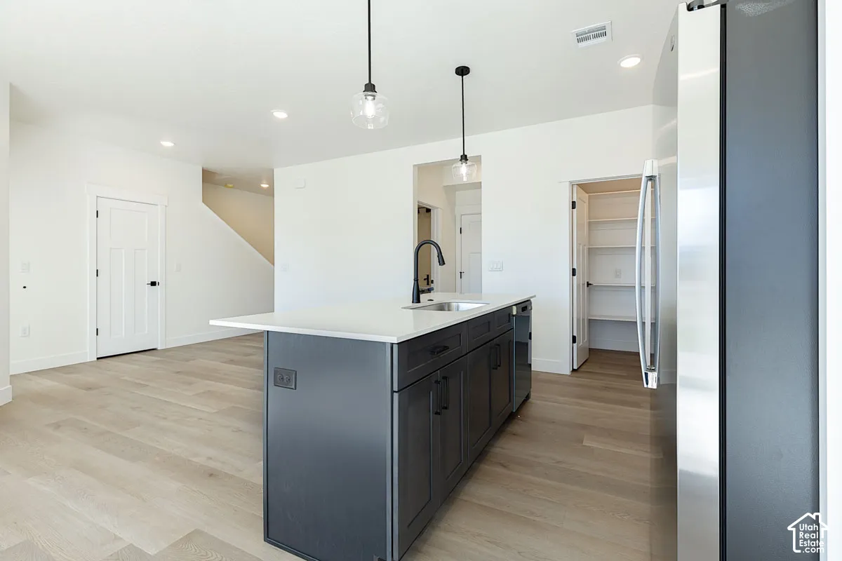 Central kitchen island with a white countertop and dark cabinetry, stainless steel refrigerator, recessed lighting, wood-finish flooring, and a walk-in pantry with built-in shelving
