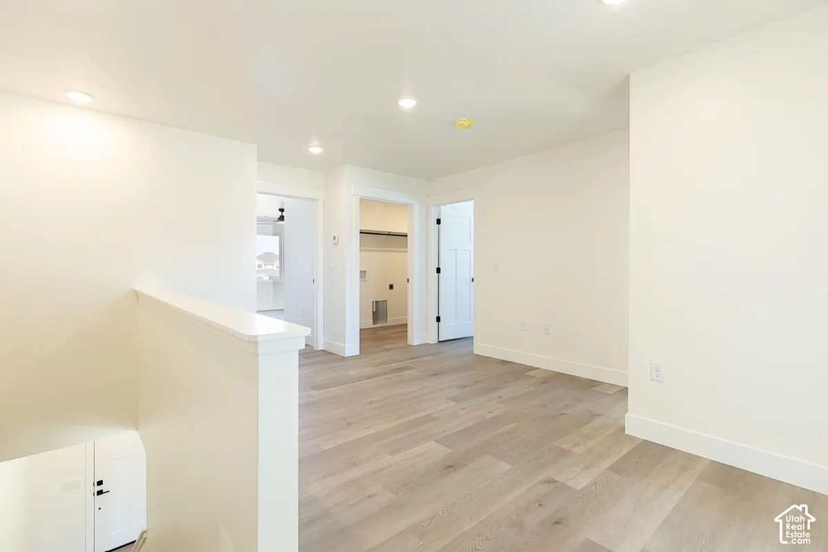 Light wood-finish flooring, recessed lighting, white interior doors, and white walls