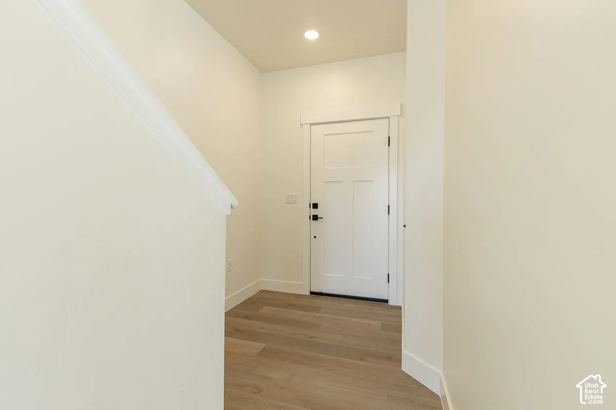 Entryway featuring wood-finish flooring, a white paneled door with black hardware, recessed lighting, and white trim