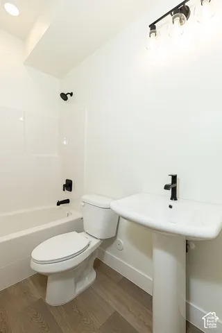 Wood-finish flooring, white pedestal sink with matte black faucet, and white tiled tub with matte black shower fixtures