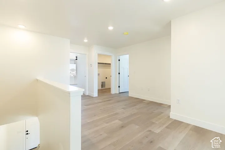 Light wood-finish flooring, recessed lighting, white interior doors, and white walls
