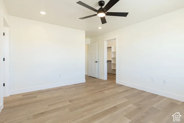 Light wood-finish flooring, white walls, black ceiling fan, recessed lighting, and a closet with built-in shelving