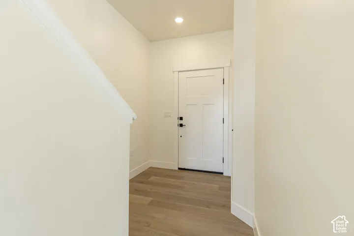 Entryway featuring wood-finish flooring, a white paneled door with black hardware, recessed lighting, and white trim