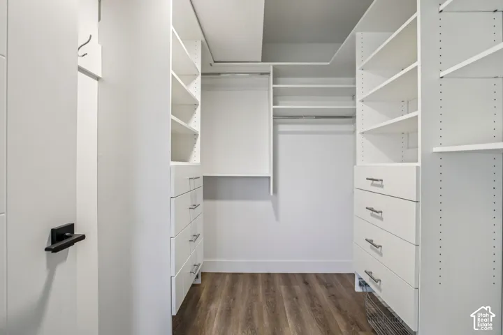 Custom built-in closet system featuring white cabinetry, multiple shelving units, integrated drawers with linear hardware, and wood-finish flooring