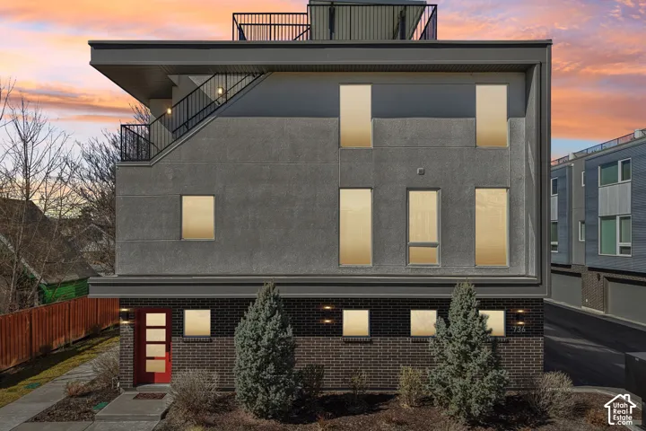 Contemporary exterior featuring a flat roofline, multi-level design, black brick facade, red entry door with frosted glass panels, and a rooftop deck with black railings
