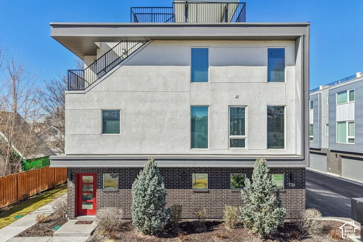 Modern exterior with a contrasting red entry door, dark brick accents, and a smooth stucco finish