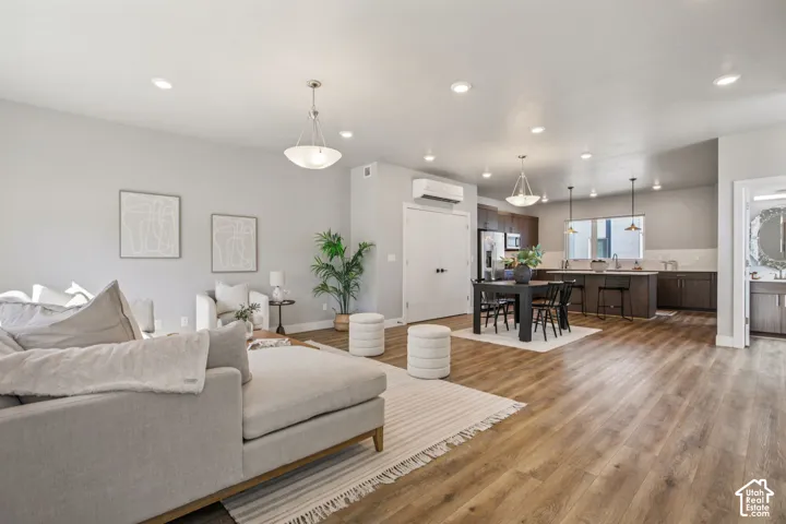 Open-concept living area featuring wood-finish flooring, recessed lighting, a modern kitchen with dark cabinetry, and a dining area with pendant lighting