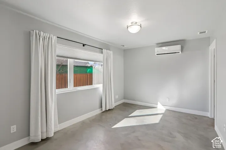 Hard-surface flooring, flush-mount ceiling light, window with white trim, wall-mounted climate control unit, and painted walls