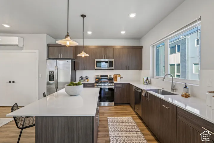 Modern kitchen featuring wood-finish flooring, white countertops, dark wood-finish cabinetry, a stainless steel gas range, and a stainless steel refrigerator