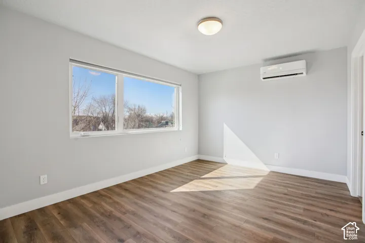 Wood-finish flooring, white baseboards, and a wall-mounted climate control unit