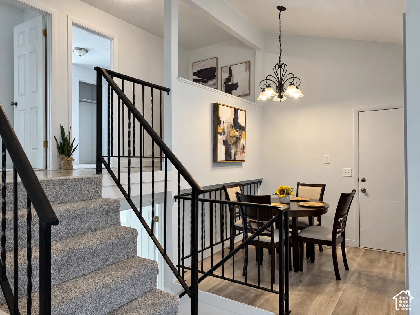 Carpeted staircase with wrought iron railing, vaulted ceiling with chandelier, and wood-finish flooring