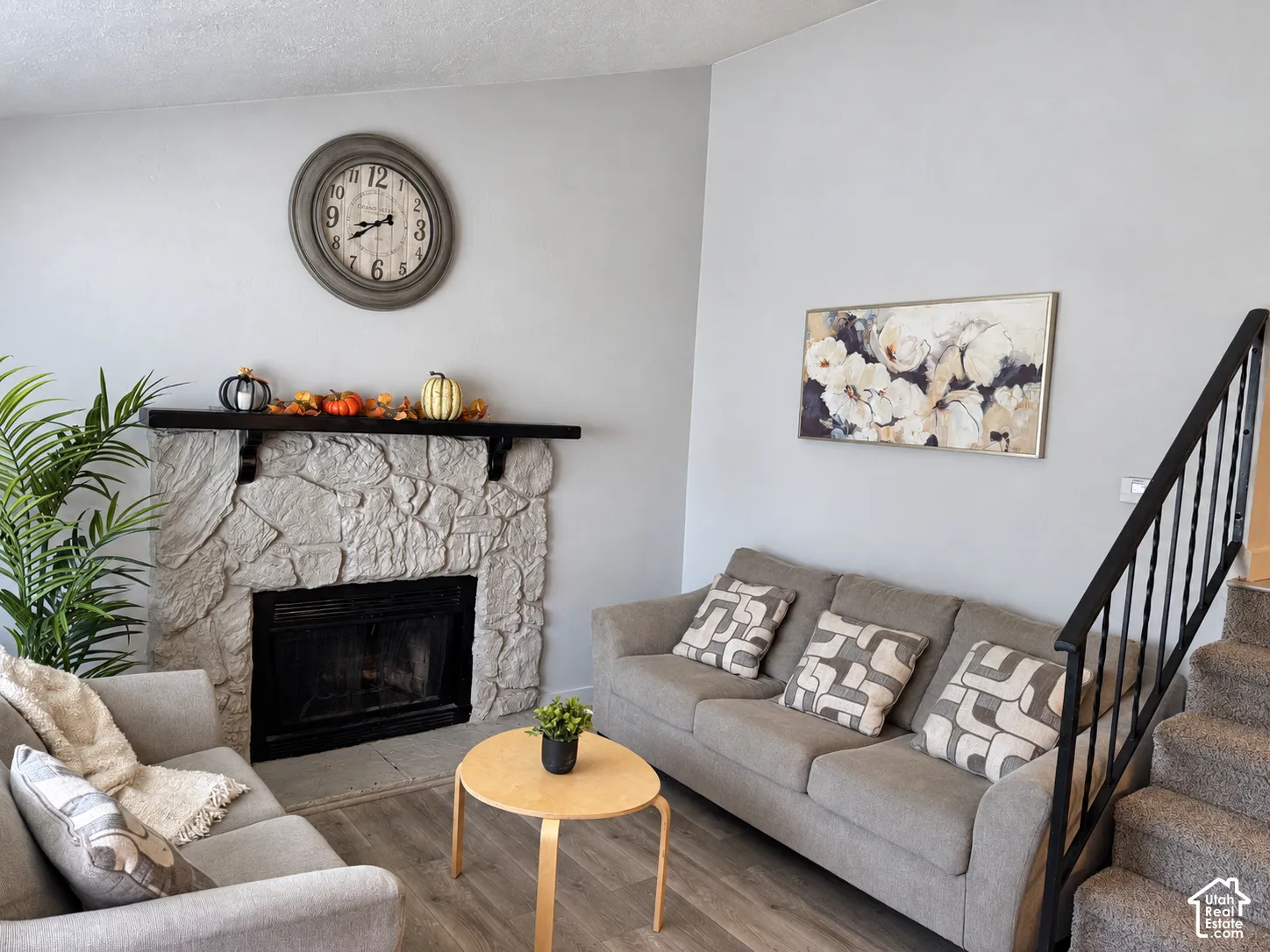 Stone-clad fireplace with a dark mantel, wood-finish flooring, and carpeted stairs with a metal railing