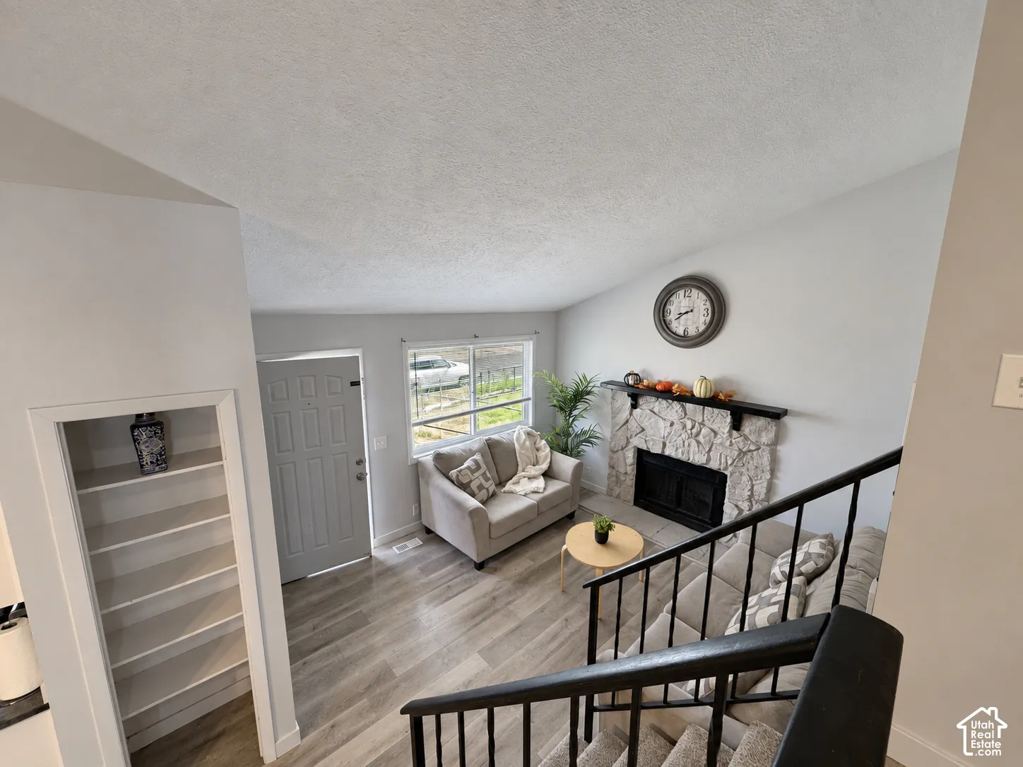 Vaulted ceiling, stone fireplace with mantel, light wood-finish flooring, built-in shelving, and black metal stair railing