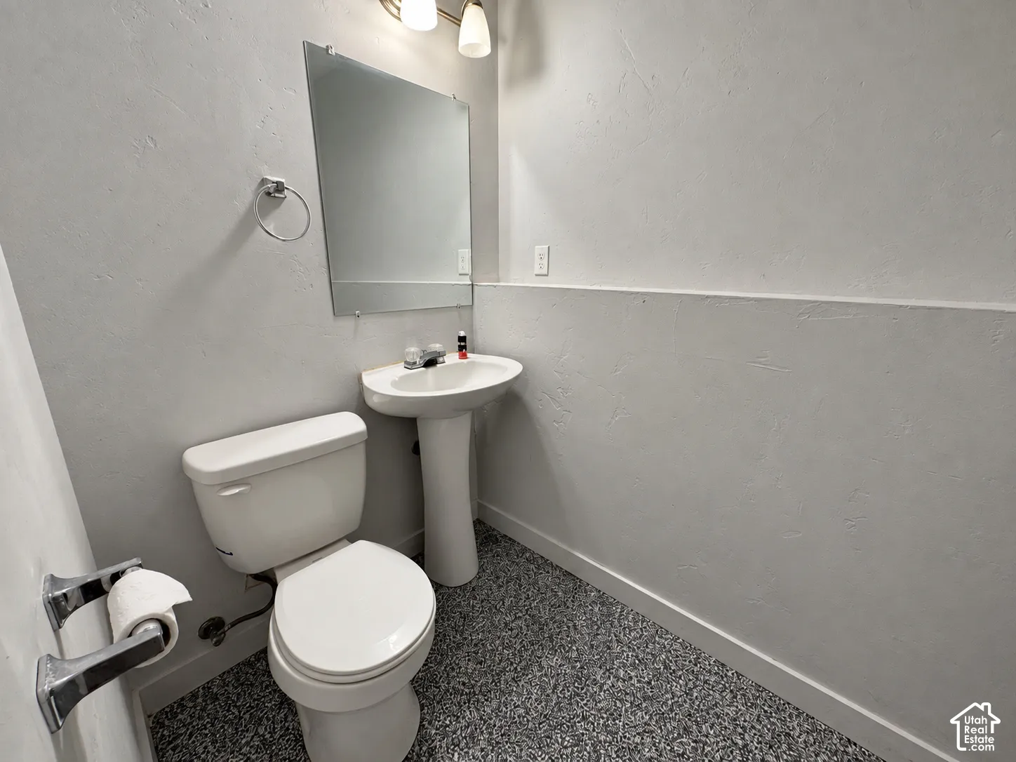 Pedestal sink with mirror, wall-mounted light fixture, and textured walls