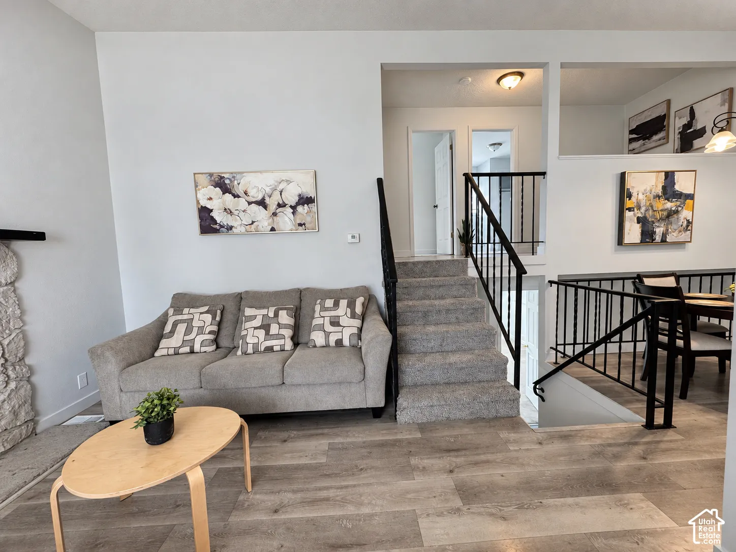 Wood-finish flooring, staircase with carpeted treads, black metal railings, and a partial stone-clad wall