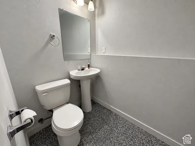 Pedestal sink with mirror, wall-mounted light fixture, and textured walls