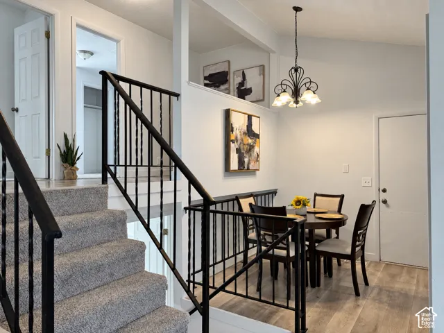 Carpeted staircase with wrought iron railing, vaulted ceiling with chandelier, and wood-finish flooring