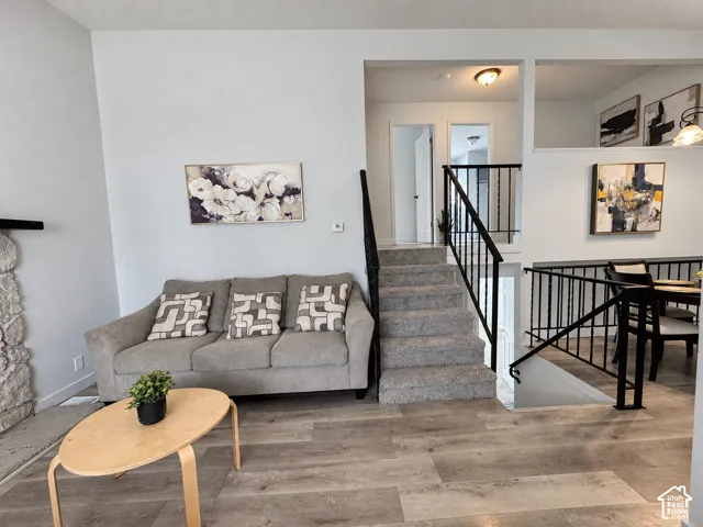 Wood-finish flooring, staircase with carpeted treads, black metal railings, and a partial stone-clad wall